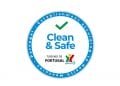 Questo è il logo della Piattaforma digitale Clean & Safe. Un logo circolare con bordo blu e segno di spunta verde all'interno. Il testo recita "Clean & Safe" con "TURISMO DE PORTUGAL" e il suo logo sotto. Il bordo riporta la dicitura "Stabilimento secondo misure sanitarie - Portogallo".