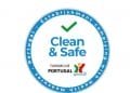 Un badge circolare con la scritta "Clean and Safe" con un segno di spunta verde sopra. Il testo che circonda il badge dice "Stabilimento conforme alle misure sanitarie - Turismo de Portugal". Vengono inoltre visualizzate l'icona di una figura colorata e le onde. Questo è il logo della Piattaforma digitale Clean & Safe.