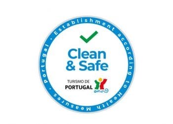 Questo è il logo della Piattaforma digitale Clean & Safe. Un logo circolare con bordo blu e segno di spunta verde all'interno. Il testo recita "Clean & Safe" con "TURISMO DE PORTUGAL" e il suo logo sotto. Il bordo riporta la dicitura "Stabilimento secondo misure sanitarie - Portogallo".