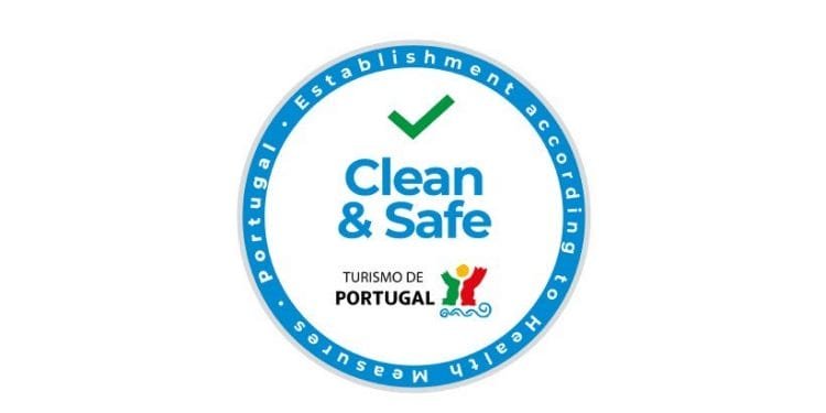Questo è il logo della Piattaforma digitale Clean & Safe. Un logo circolare con bordo blu e segno di spunta verde all'interno. Il testo recita "Clean & Safe" con "TURISMO DE PORTUGAL" e il suo logo sotto. Il bordo riporta la dicitura "Stabilimento secondo misure sanitarie - Portogallo".