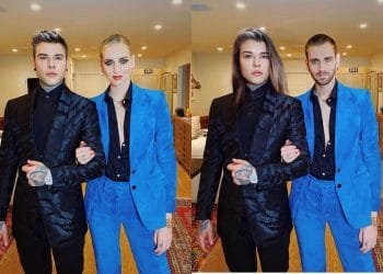 Immagine elaborata con FaceApp. Due coppie di individui posano per una foto in un ambiente moderno. Ogni coppia include una persona in abito blu con una camicia nera e un'altra in abito nero. Entrambe le coppie stanno a braccetto, con espressioni sicure. Sul pavimento è visibile un tappeto.