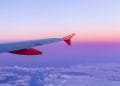 Vista dal finestrino di un aereo che mostra un vivace cielo al tramonto rosa e viola. L'ala e l'ala dell'aereo, marchiate con "easyJet" in testo bianco su sfondo arancione, si estendono nell'inquadratura, con le nuvole visibili sotto.