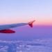Vista dal finestrino di un aereo che mostra un vivace cielo al tramonto rosa e viola. L'ala e l'ala dell'aereo, marchiate con "easyJet" in testo bianco su sfondo arancione, si estendono nell'inquadratura, con le nuvole visibili sotto.
