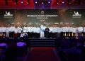 Un folto gruppo di chef in giacca bianca è sul palco alla cerimonia delle premiazioni Guida Michelin Portogallo 2025. L' omino Michelin è al centro, circondato dai premiati. Lo sfondo mostra il logo Michelin e vari loghi degli sponsor, mentre il pubblico è seduto di fronte.