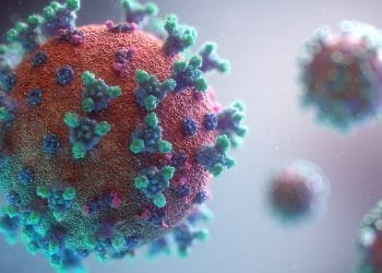 Un'immagine 3D ravvicinata di una particella virale. Il virus sferico ha una superficie strutturata di colore arancione ed è ricoperto di proteine spike di colore verde e viola. Lo sfondo è sfocato con ulteriori particelle virali che fluttuano in lontananza.