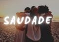 Quattro persone che si abbracciano su una spiaggia durante il tramonto. La parola "SAUDADE" è ben visibile in grassetto bianco sull'immagine.