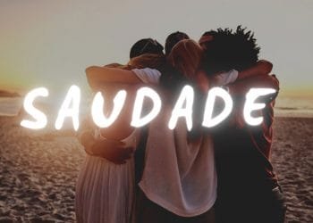 Quattro persone che si abbracciano su una spiaggia durante il tramonto. La parola "SAUDADE" è ben visibile in grassetto bianco sull'immagine.