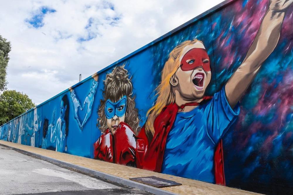 dipinto su muro principalmente di colore blu, raffigurante due bambini con la maschera e alcuni infermieri