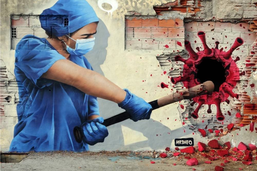 dipinto su muro raffigurante una infermiera con una mazza da baseball che colpisce una rappresentazione iconografica del virus