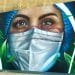 Un murale raffigura il primo piano di una donna che indossa un berretto chirurgico blu e una maschera bianca. I suoi occhi espressivi suggeriscono un'espressione seria. Intorno a lei ci sono rose bianche e foglie verdi che aggiungono un tocco di natura all'opera d'arte.