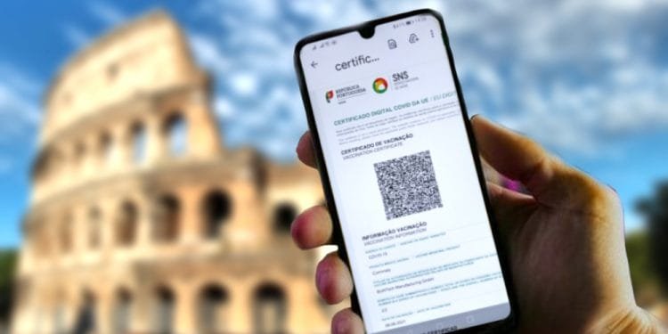 Una mano che tiene uno smartphone su cui è visualizzato un certificato di vaccinazione digitale con un codice QR davanti all'iconico Colosseo di Roma in una giornata soleggiata con cielo parzialmente nuvoloso.