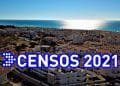 Una città costiera con numerosi edifici bianchi sotto un cielo limpido. Il sole sta tramontando o sorgendo sull'oceano calmo sullo sfondo. Il testo sovrapposto recita "Censos 2021" in grandi lettere blu e bianche.