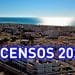 Una città costiera con numerosi edifici bianchi sotto un cielo limpido. Il sole sta tramontando o sorgendo sull'oceano calmo sullo sfondo. Il testo sovrapposto recita "Censos 2021" in grandi lettere blu e bianche.