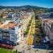 Una vivace veduta aerea di una città con una lunga strada pedonale fiancheggiata da fiori fiancheggiata da edifici storici con tetti di tegole rosse. Uno scenario scenografico di colline si estende in lontananza. Fiori gialli brillanti dominano il percorso centrale e si vedono persone passeggiare: una scena perfetta per investire in Portogallo.