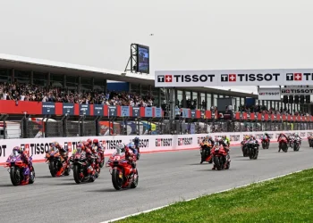 I motociclisti sfrecciano lungo la pista dell'Autódromo Internacional do Algarve, circondati dagli spettatori sugli spalti. Il circuito presenta il marchio Tissot su striscioni e strutture. I motociclisti indossano equipaggiamento colorato e la pista è fiancheggiata da erba.