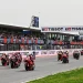 I motociclisti sfrecciano lungo la pista dell'Autódromo Internacional do Algarve, circondati dagli spettatori sugli spalti. Il circuito presenta il marchio Tissot su striscioni e strutture. I motociclisti indossano equipaggiamento colorato e la pista è fiancheggiata da erba.