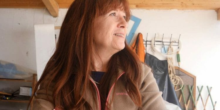 Manuela Quintavalle, una donna dai lunghi capelli castano-rossastri, sta in casa, sorride e guarda di lato. Indossa una giacca beige e ha le braccia incrociate. Dietro di lei, vari strumenti e oggetti sono disposti su scaffali e sul soffitto è visibile una trave di legno.