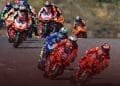 Diversi motociclisti in tute da corsa colorate e caschi percorrono una pista sulle loro moto ad alta velocità durante una gara competitiva del Moto GP Portogallo. I primi due corridori viaggiano su bici rosse, seguiti da vicino da altri su bici di vari colori. Lo sfondo è sfocato.
