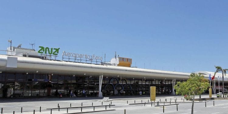 Immagine dell'esterno dell'aeroporto di Faro. L'edificio presenta un grande cartello con la scritta "Aeroporto de Faro" insieme a un logo verde. Il cielo è limpido e azzurro e il traffico veicolare e pedonale davanti al terminal è minimo. Questo vivace hub è anche conosciuto come Aeroporto Gago Coutinho.