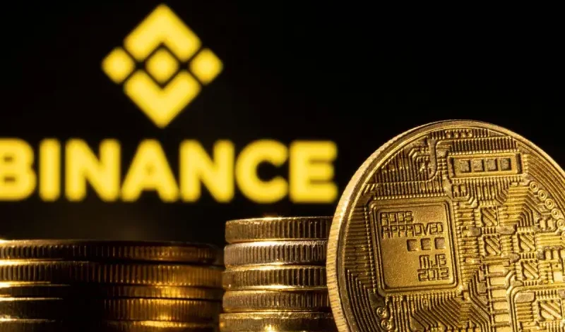 In primo piano si vedono pile di monete color oro con disegni simili a circuiti, mentre sullo sfondo compaiono il logo e il nome Binance sfocati in giallo, simili a quelli discussi al Crypto Portogallo Web Summit.