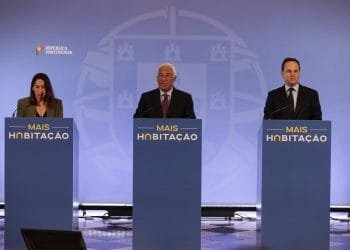 Tre persone stanno dietro i podi durante una conferenza stampa. I podi hanno la scritta "MAIS HABITAÇÃO" e lo sfondo include il logo e il testo "REPÚBLICA PORTUGUESA". Le persone sembrano rivolgersi al pubblico riguardo alle misure abitazione.