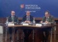 Tre uomini sono seduti al tavolo di una sala conferenze. L'uomo al centro parla al microfono, mentre gli altri due ascoltano attentamente. Sul fondale sono presenti il logo e il nome della "República Portuguesa" e "Economia e Mar", oltre ai riferimenti all'ASAE controlli prezzi scritti in portoghese.