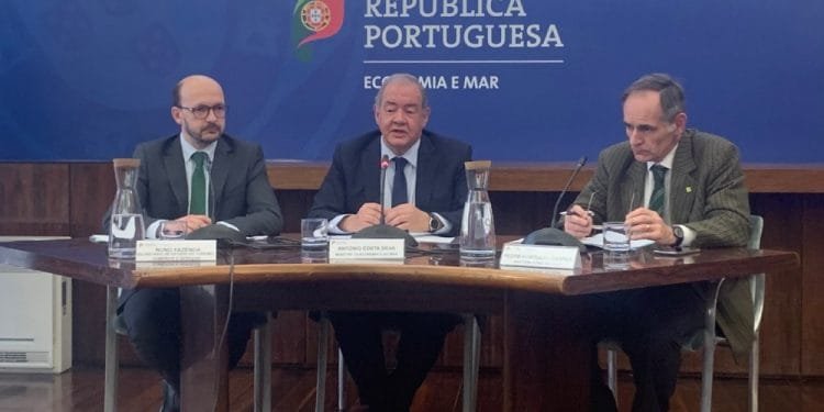Tre uomini sono seduti al tavolo di una sala conferenze. L'uomo al centro parla al microfono, mentre gli altri due ascoltano attentamente. Sul fondale sono presenti il logo e il nome della "República Portuguesa" e "Economia e Mar", oltre ai riferimenti all'ASAE controlli prezzi scritti in portoghese.