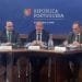 Tre uomini sono seduti al tavolo di una sala conferenze. L'uomo al centro parla al microfono, mentre gli altri due ascoltano attentamente. Sul fondale sono presenti il logo e il nome della "República Portuguesa" e "Economia e Mar", oltre ai riferimenti all'ASAE controlli prezzi scritti in portoghese.