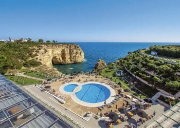 Una veduta aerea di un resort costiero caratterizzato da una grande piscina circolare con una piscina più piccola adiacente, circondata da sedie a sdraio e ombrelloni. Il resort si affaccia su una scogliera e sull'oceano blu, con una vegetazione lussureggiante e alcuni edifici sullo sfondo: davvero il migliore gennaio degli ultimi 20 anni.