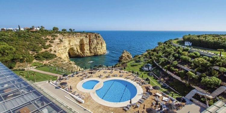 Una veduta aerea di un resort costiero caratterizzato da una grande piscina circolare con una piscina più piccola adiacente, circondata da sedie a sdraio e ombrelloni. Il resort si affaccia su una scogliera e sull'oceano blu, con una vegetazione lussureggiante e alcuni edifici sullo sfondo: davvero il migliore gennaio degli ultimi 20 anni.