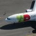 Un grande aereo commerciale con la scritta "Portogallo" e un logo sul lato è parcheggiato sulla pista dell'aeroporto. Una persona con un giubbotto di sicurezza giallo cammina accanto all'aereo TAP, che ha segni verdi, rossi e gialli sulla fusoliera e sulle ali. Sono visibili i segni del terreno, che ricordano i colori vivaci del loro bilancio 2022.