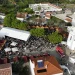 Vista aerea di un affollato del Festival del Folar dolce pasquale portoghese a Silves. Immagine all'aperto con tende bianche e tettoie arancioni tra edifici bianchi, tra cui una chiesa, dove i visitatori possono gustare prelibatezze come il Folar, circondati dal verde e dai veicoli parcheggiati.