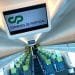 Interno di una moderna cabina ferroviaria con file di sedili blu e verdi ben organizzati. In alto, un display digitale mostra "CP" e "Comboios de Portugal", che indicano l'operatore ferroviario. Grandi finestre fiancheggiano le pareti, consentendo alla luce naturale di entrare nella cabina pulita e ben illuminata: davvero utile e positivo.