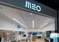 Un negozio moderno e luminoso con l'insegna "MEO" sopra l'ingresso. Il negozio presenta scaffali in legno lungo le pareti, che espongono vari dispositivi elettronici e accessori, tutti provenienti da Altice Portugal. Display multipli completano un bancone centrale del servizio clienti.