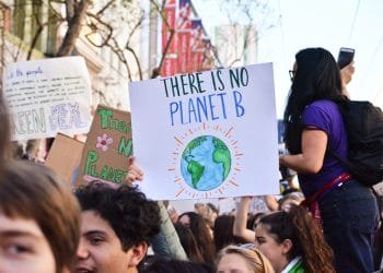 Un folto gruppo di persone partecipa a una protesta contro il cambiamento climatico. Una persona tiene in mano un cartello con l'illustrazione della Terra e la scritta "Non esiste un pianeta B". Altri cartelli, come “Studenti contro i cambiamenti climatici”, sono visibili sullo sfondo. L'atmosfera appare energica e impegnata.