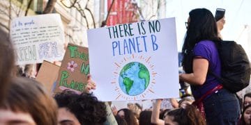 Un folto gruppo di persone partecipa a una protesta contro il cambiamento climatico. Una persona tiene in mano un cartello con l'illustrazione della Terra e la scritta "Non esiste un pianeta B". Altri cartelli, come “Studenti contro i cambiamenti climatici”, sono visibili sullo sfondo. L'atmosfera appare energica e impegnata.