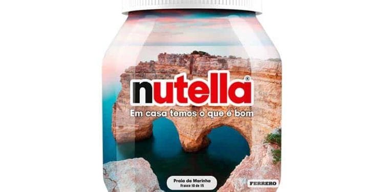 Un barattolo di Nutella con l'immagine di Praia da Marinha, una spiaggia pittoresca nella regione portoghese dell'Algarve con scogliere frastagliate e un arco naturale, sull'etichetta. Il testo sull'etichetta dice "Em casa temos o que é bom" e "Praia da Marinha", insieme al logo Ferrero.