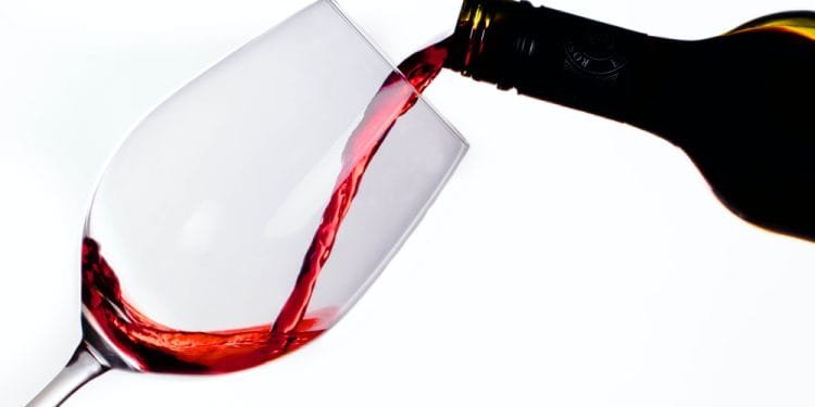 Una bottiglia di vino rosso viene versata in un bicchiere di vino trasparente inclinato su uno sfondo bianco. Il vino, che ricorda il Portogallo alto consumo vino, è a metà, creando un flusso che riempie il bicchiere.