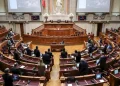 Camera legislativa con numerosi posti disposti a semicerchio. Diverse persone stanno in piedi e conversano nella stanza, probabilmente discutendo di recenti decisioni come quando la legge eutanasia è stata approvata in Portogallo. Sullo sfondo sono visibili grandi schermi e statue, insieme a un prominente podio per oratori nella parte anteriore.