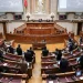 Camera legislativa con numerosi posti disposti a semicerchio. Diverse persone stanno in piedi e conversano nella stanza, probabilmente discutendo di recenti decisioni come quando la legge eutanasia è stata approvata in Portogallo. Sullo sfondo sono visibili grandi schermi e statue, insieme a un prominente podio per oratori nella parte anteriore.