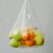 Un sacchetto di plastica trasparente pieno di frutta assortita, tra cui mele verdi e gialle, arance e una banana, è sospeso su un semplice sfondo grigio chiaro. I colori vivaci dei frutti sono visibili attraverso la plastica, evidenziando la necessità di prendere in considerazione iniziative di divieto sacchetti plastica.