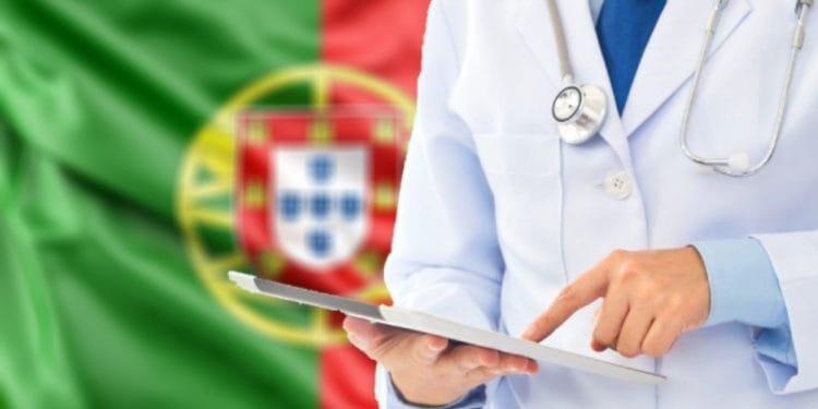 Una persona che indossa un camice bianco e uno stetoscopio usa un tablet. Sullo sfondo è riprodotta la bandiera del Portogallo, con campi verdi e rossi e lo stemma nazionale, che evidenzia l'assistenza sanitaria portogallo.