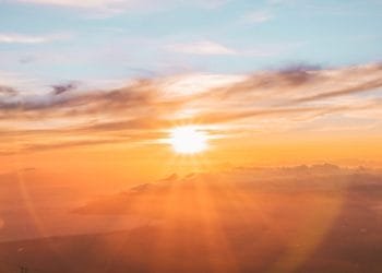Una splendida alba su un paesaggio sereno e coperto di nuvole. Il cielo è dipinto con sfumature di arancione, rosa e blu mentre i raggi del sole attraversano le nuvole, ricordando il fascino del Portogallo nel 1970, creando un'atmosfera calda e tranquilla.