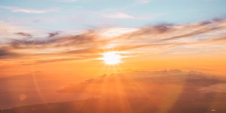 Una splendida alba su un paesaggio sereno e coperto di nuvole. Il cielo è dipinto con sfumature di arancione, rosa e blu mentre i raggi del sole attraversano le nuvole, ricordando il fascino del Portogallo nel 1970, creando un'atmosfera calda e tranquilla.