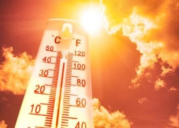 Un termometro mostra sia la scala Celsius che quella Fahrenheit con temperature superiori a 40°C (104°F), sullo sfondo di un cielo luminoso e soleggiato con nuvole sparse. L'intensa luce solare e le tonalità giallo-arancio suggeriscono condizioni climatiche molto calde, che ricordano una giornata torrida nel Caldo Portogallo.