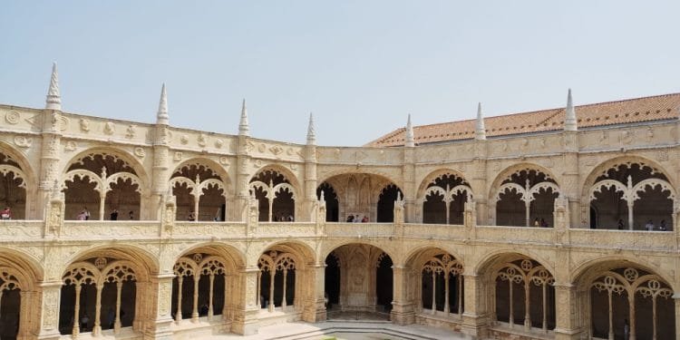 Un ampio cortile in pietra finemente scolpito con passaggi ad arco e guglie decorative, caratterizzato da un prato verde ben curato al centro. Il chiostro a due piani, spesso accessibile durante l'"ingresso gratuito musei portoghesi", vanta un design architettonico caratteristico degli stili gotico e manuelino.