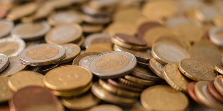 Una grande pila di monete diverse è sparsa su una superficie. Le monete sono di diverse dimensioni, valori e colori, con diverse monete da due euro e una Giornata Gioventù monetaria commemorativa visibili vicino al centro. L'immagine cattura un vasto assortimento di valute in una disposizione sciolta e disorganizzata.