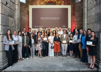 Un gruppo di persone, vestite con abiti business casual, sta in posa per la premiazione Best Of Wine Tourism in Porto 2026, tenendo in mano i diplomi. La foto è scattata al chiuso tra due imponenti muri e difronte ad un maxischermo.
