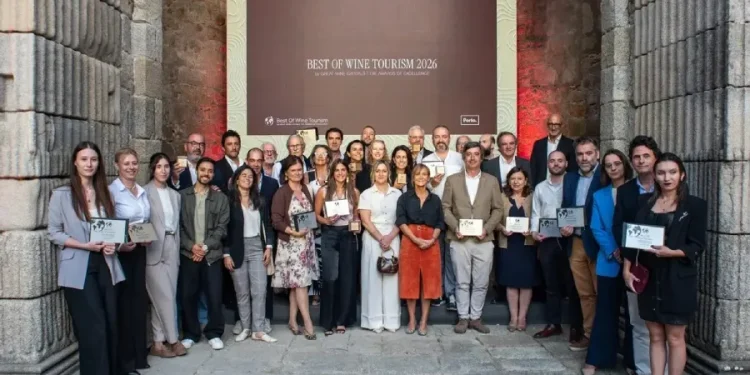 Un gruppo di persone, vestite con abiti business casual, sta in posa per la premiazione Best Of Wine Tourism in Porto 2026, tenendo in mano i diplomi. La foto è scattata al chiuso tra due imponenti muri e difronte ad un maxischermo.