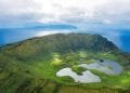 Veduta aerea del cratere vulcanico dell'isola di Corvo nelle Azzorre, Portogallo. Il vasto cratere verde è punteggiato da piccoli laghi e circondato dal blu dell'Oceano Atlantico, con un'altra isola visibile in lontananza sotto un cielo parzialmente nuvoloso: una straordinaria novità voli Azzorre.